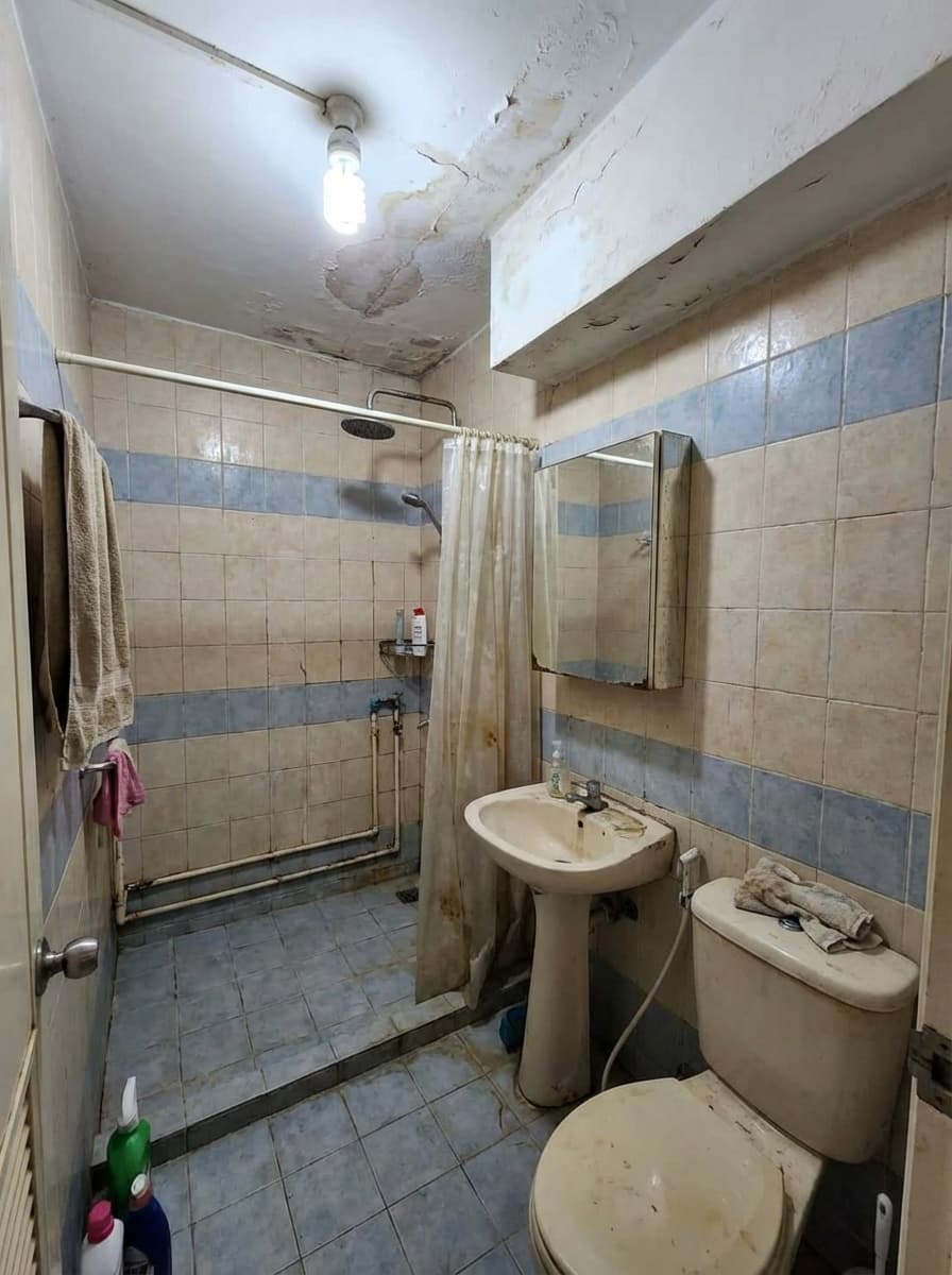 Old bathroom with damaged ceiling and outdated fixtures